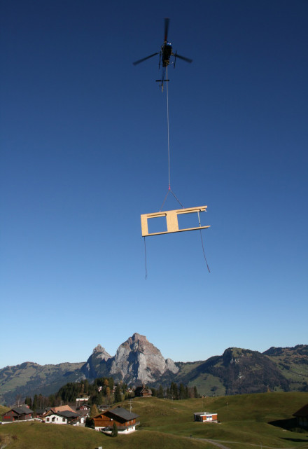 Un hélicoptère survole Stoos avec un élément de paroi. 